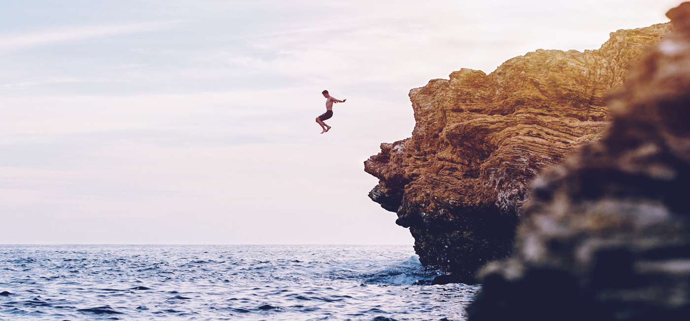 man jumping off a cliff into water